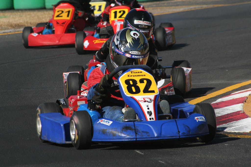 Dynamic go kart racing action on a track with multiple racers in vibrant karts wearing helmets.